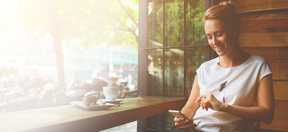 Woman in coffee shop reading email on smartphone