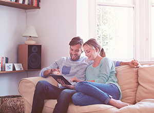 Forwarddarlehen: Junges Paar sitzt mit ihren Tablett auf dem Sofa