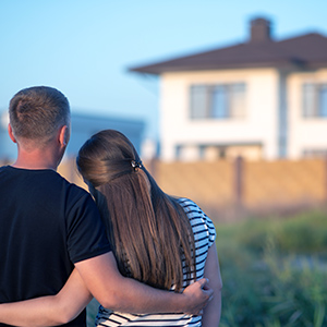 Bausparvertrag: Junges Paar schaut auf Haus im Hintergrund