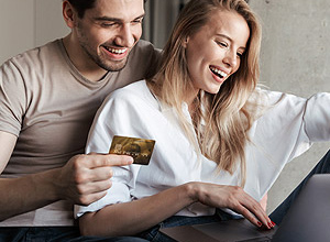 Kreditkarte: Junges Paar sitzt mit ihrem Laptop auf dem Sofa