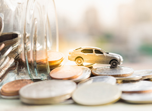 Autofinanzierung: Modellauto fährt auf Münzen aus einem gekippten Glas