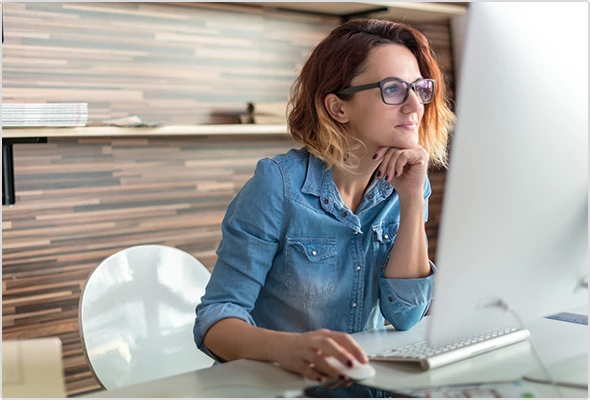 Frau, die vor Ihrem Rechner sitzt und mit der Computermaus in der Hand etwas erledigt