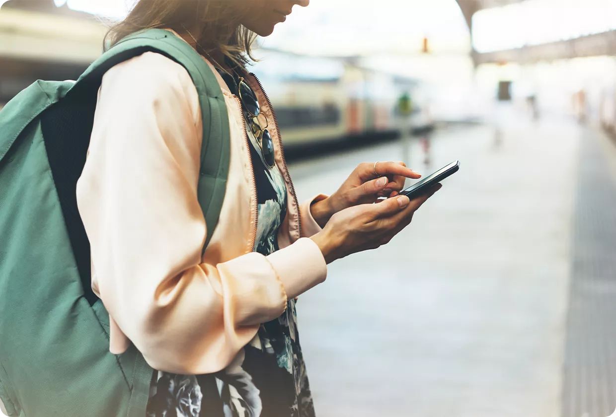 Frau steht auf dem Bahnsteig und tippt auf ihrem Handy