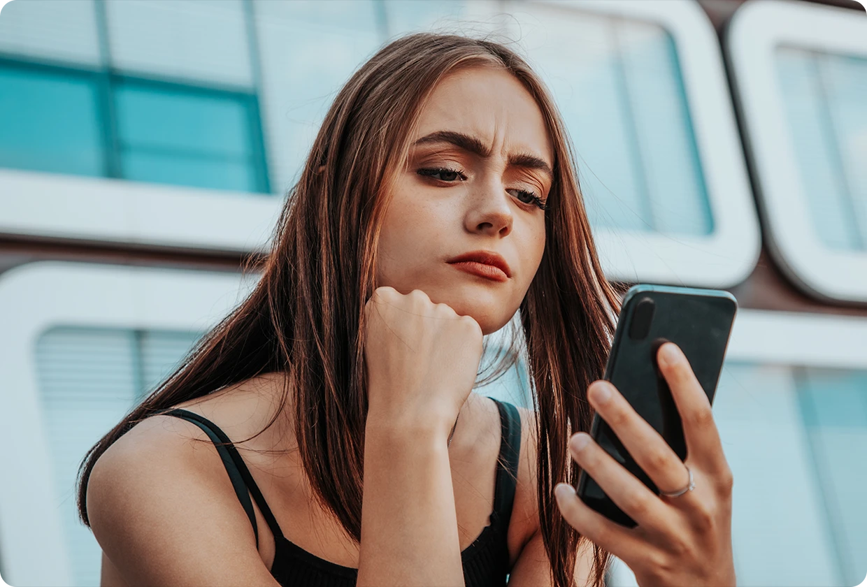 Junge Frau schaut stirnrunzelnd auf ihr Handy.