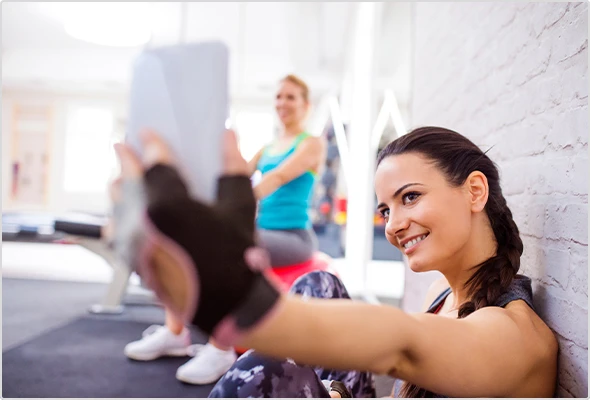 Junge Frau nimmt ein Selfie im Fitnessstudio auf. Im Hintergrund weitere Menschen.