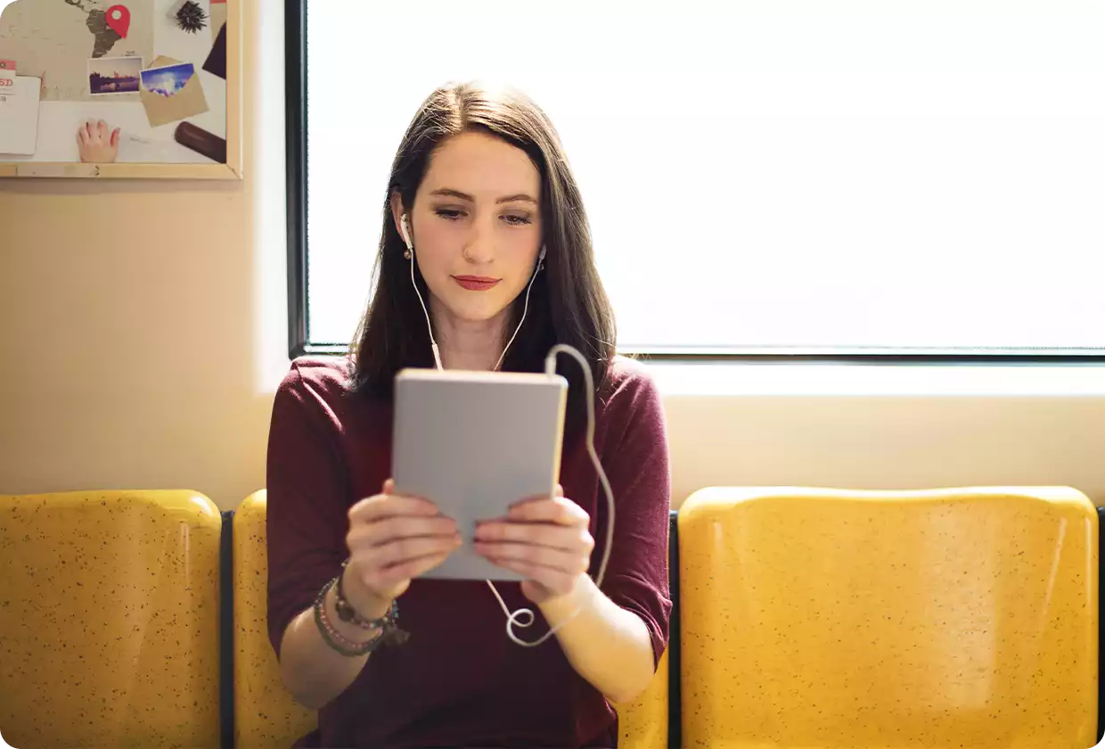 Junge Frau mit Tablet und Kopfhörern schaut auf Display.