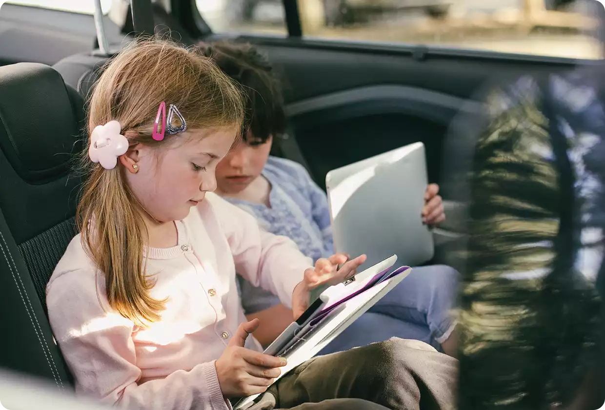 Zwei Kinder im Auto, die ein Tablet bedienen