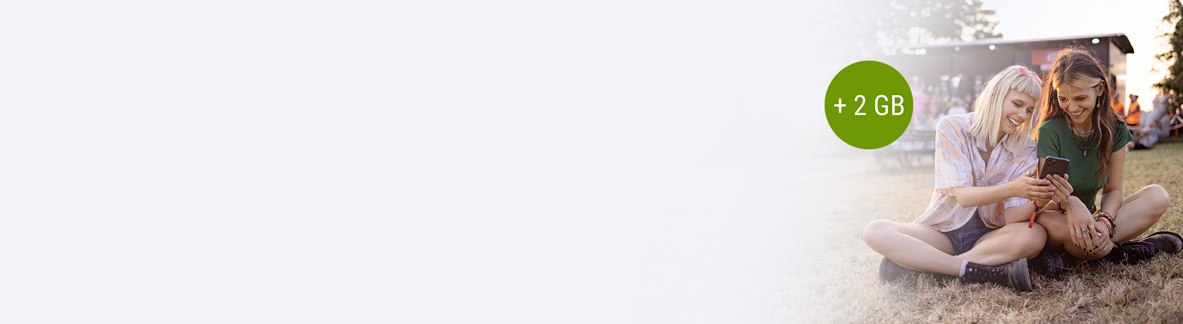 Zwei Frauen sitzen mit Handy auf der Wiese