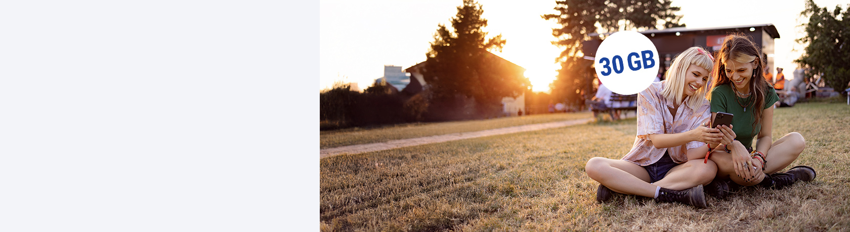 Zwei Frauen sitzen mit Handy auf der Wiese