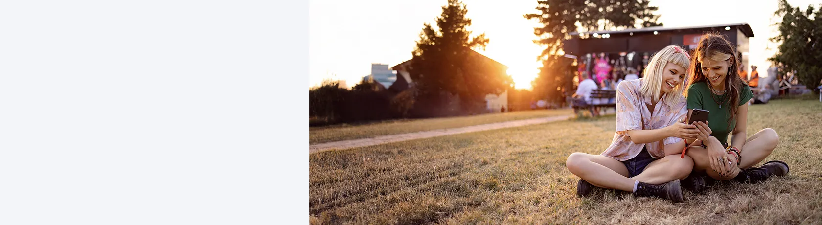 Zwei Frauen sitzen mit Handy auf der Wiese
