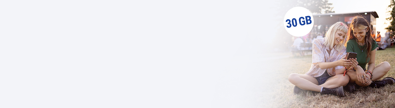 Zwei Frauen sitzen mit Handy auf der Wiese