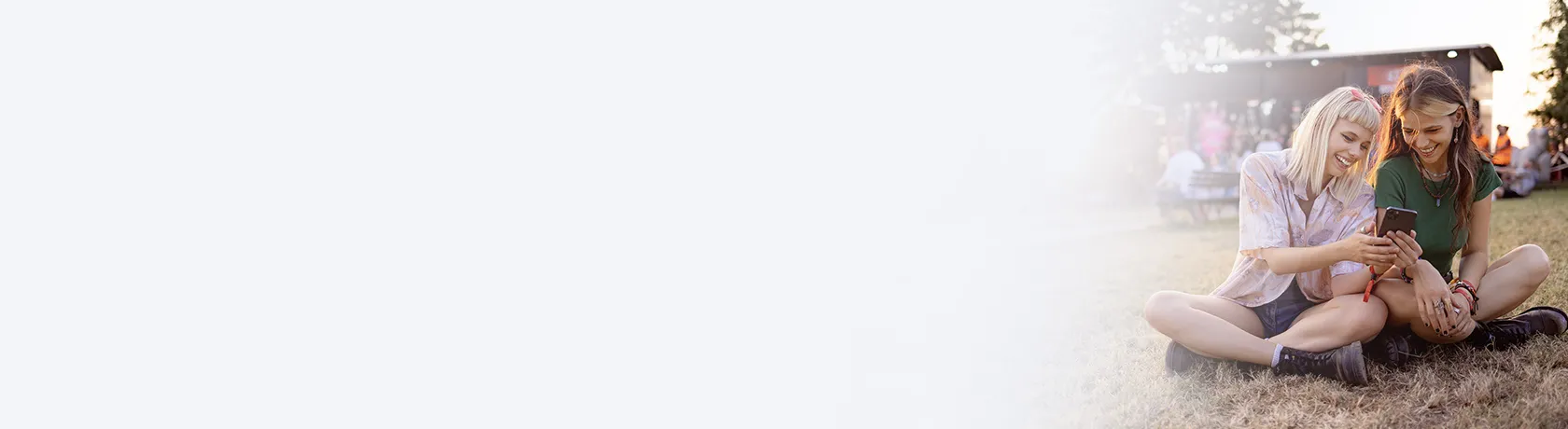 Zwei Frauen sitzen mit Handy auf der Wiese