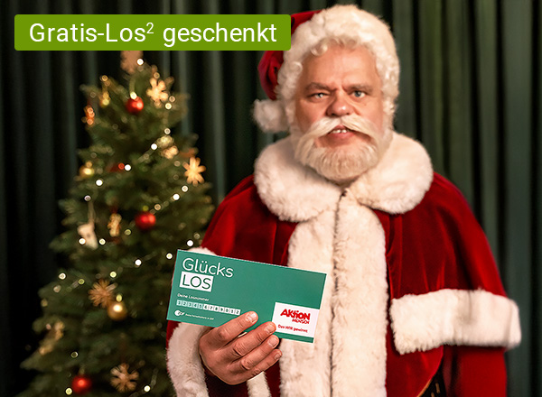 Person in rotem Weihnachtsmannkostüm hält ein grünes Los mit der Aufschrift 'Glücks LOS' vor einem geschmückten Weihnachtsbaum.