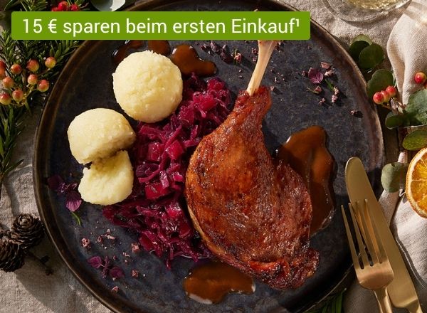 Gebratene Gänsekeule mit Rotkohl, Klößen und Soße auf dunklem Teller, festlich serviert.