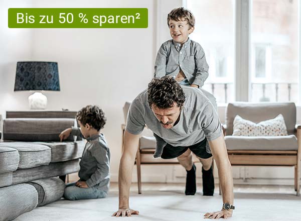 Ein Mann macht Liegestütze im Wohnzimmer, während ein Kind in der Nähe spielt uns eines auf seinem Rücken sitzt, oben links in der Ecke ist der hinweis geschrieben, dass man jetzt bei Cosmos Direkt 50 % sparen kann auf die Unfallversicherung²