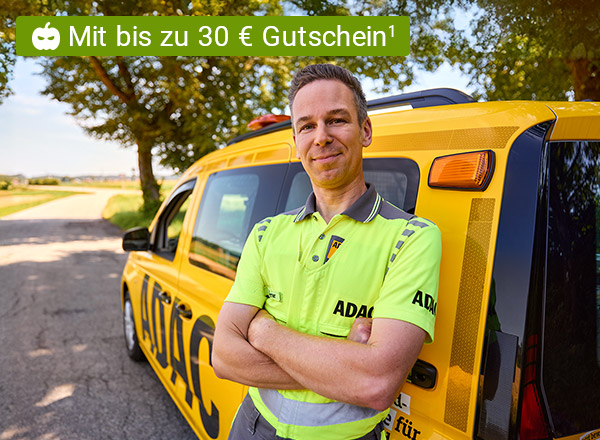 ADAC-Mitarbeiter in gelbem Polo steht vor gelbem Pannenhilfsfahrzeug auf Landstraße, Text 'Mit bis zu 30 € Gutschein'