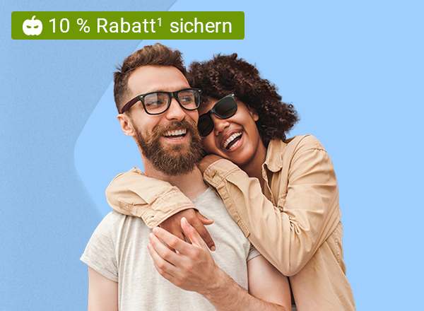 Ein Mann und eine Frau, welche beide lächeln und die Frau umarmt den Mann von Hinten seitlich. Der Mann trägt eine Brille mit einem schwarzen Rahmen und die Frau trägt eine schwarze Sonnenbrille.