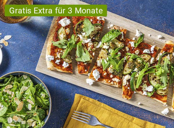 Flammkuchen auf einem Holzbrett, danben gelbe Serviette mit Gabel darauf und eine Schüssel mit grünem Salat. Mit Chiptext: Gratis Extra für 3 Monate