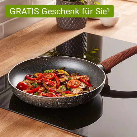 Bratpfanne mit Holzgriff auf Herd, gefüllt mit gebratenem Gemüse wie Tomaten, Paprika und Pilzen, dazu ein Chip mit dem Text: GRATIS Geschenk für Sie¹
