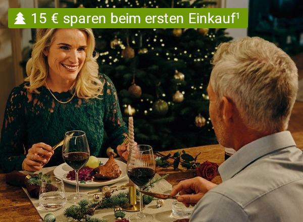Zwei Personen feiern fröhlich beim Weihnachtsessen mit Wein und festlich gedecktem Tisch.
