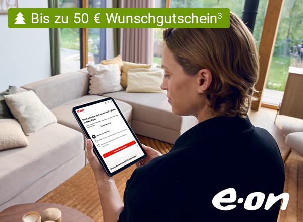 Person mit braunen Haaren hält Tablet mit E.ON-Webseite, sitzt vor hellgrauem Sofa mit Kissen in hellem Wohnzimmer.