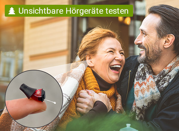 Ein grauhaariger Mann und eine rothaarige Frau sitzen lachend vor einem Haus. Der Mann hat die Frau im Arm. In einer Nahaufnahme ist ein Hörgerät zu sehen, das mit einem Pfeil auf das Ohr der Frau zeigt. Zudem wir in einem schriftlichen Hinweis darauf verwiesen, das man das beworben Hörgerät von proauris kostenlos testen kann.