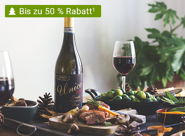 Flasche Rotwein mit goldener Kapsel und schwarzem Etikett 'Unico', daneben Weinglas mit Rotwein, grüne Trauben und Tannenzapfen auf Tisch.