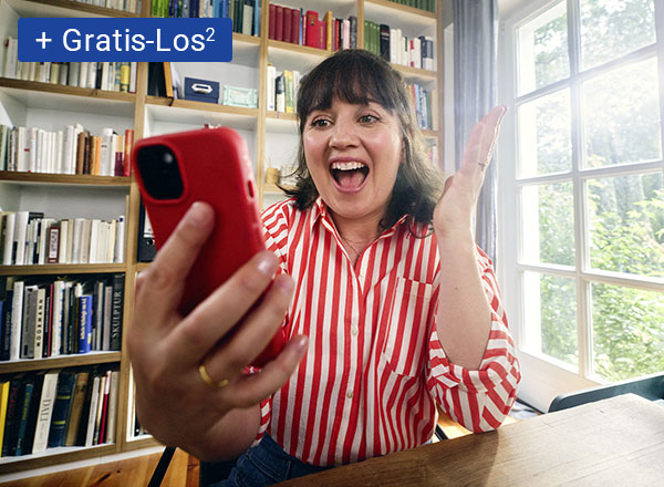 Person mit gestreiftem Hemd hält rotes Smartphone vor Bücherregal und hebt die Hand