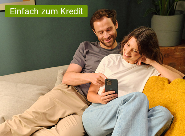 Zwei Personen sitzen entspannt auf einem Sofa, eine hält ein Smartphone, im Hintergrund steht ein Blumentopf auf einem Holzmöbel.