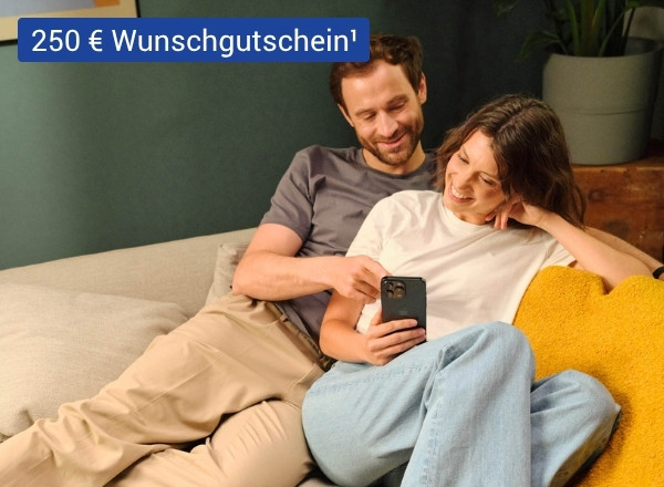 Zwei Personen sitzen entspannt auf einem Sofa, eine hält ein Smartphone, im Hintergrund steht ein Blumentopf auf einem Holzmöbel.