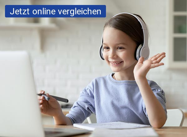 Ein junges Mädchen sitzt mit Kopfhörern an einem Tisch und hat einen Stift in der Hand. Vor ihr liegt ein weißer Block und es steht schräg vor ihr ein silbernen Laptop, auf welchen sie schaut und winkt.