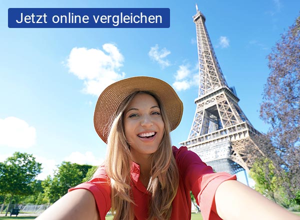 Eine junge Frau macht ein Selfie vor dem Eifelturm in Frankreich. Der Himmel strahlt blau mit ein paar vereinzelten Wolken.