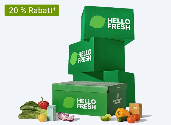 Drei grüne HelloFresh-Lieferboxen gestapelt mit einer weiteren Box im Vordergrund, daneben frisches Gemüse und Obst.