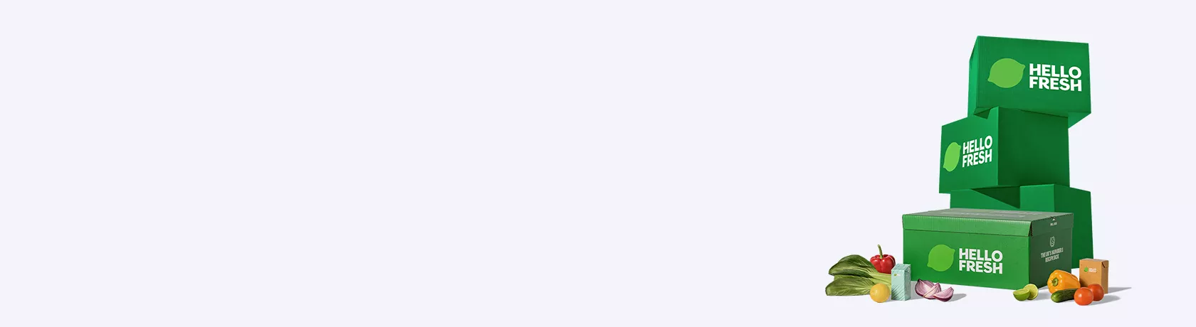 Drei grüne HelloFresh-Lieferboxen gestapelt mit einer weiteren Box im Vordergrund, daneben frisches Gemüse und Obst.