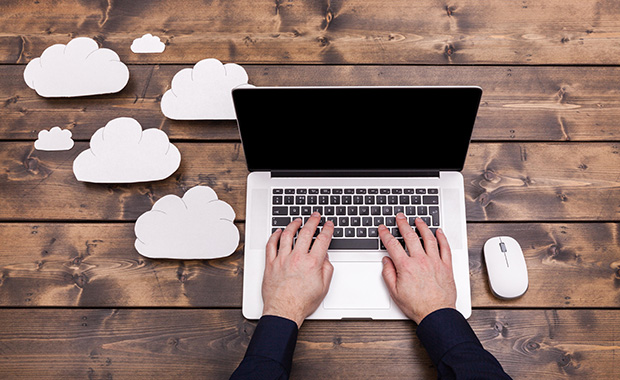 Hands type on laptop surrounded by cloud icons