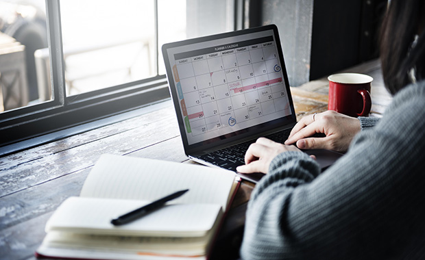 Laptop on wood surface with calendar on screen and typing hands