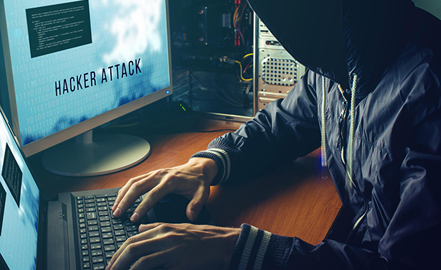 Person wearing hoodie types on laptop while looking at screen with the words Hacker Attack