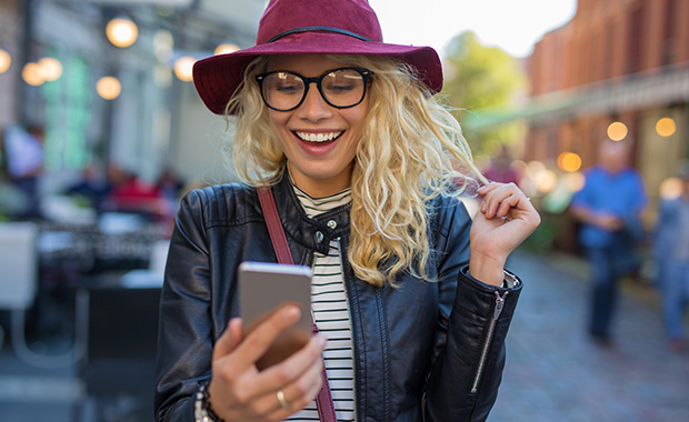 Woman in hat smiles while looking at iPhone