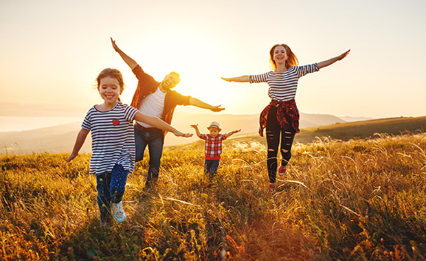 Family of four runs through field of grain at sunset