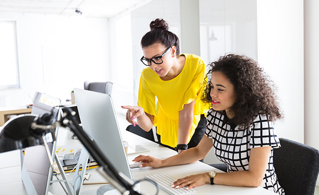 Two young businesswomen working together in the office at a computer