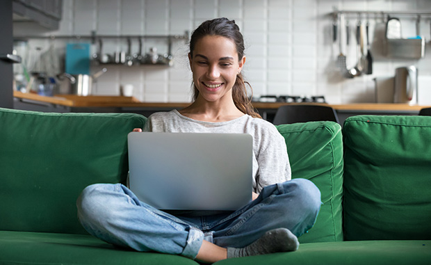 Smiling young woman on sofa holding laptop