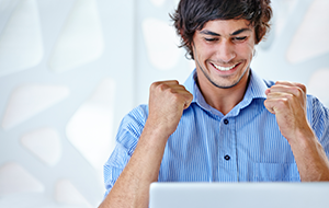 An ecstatic young businessman wearing a blue shirt sitting in front of his laptop