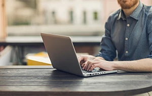 Person works on laptop on wooden table their face is not visible