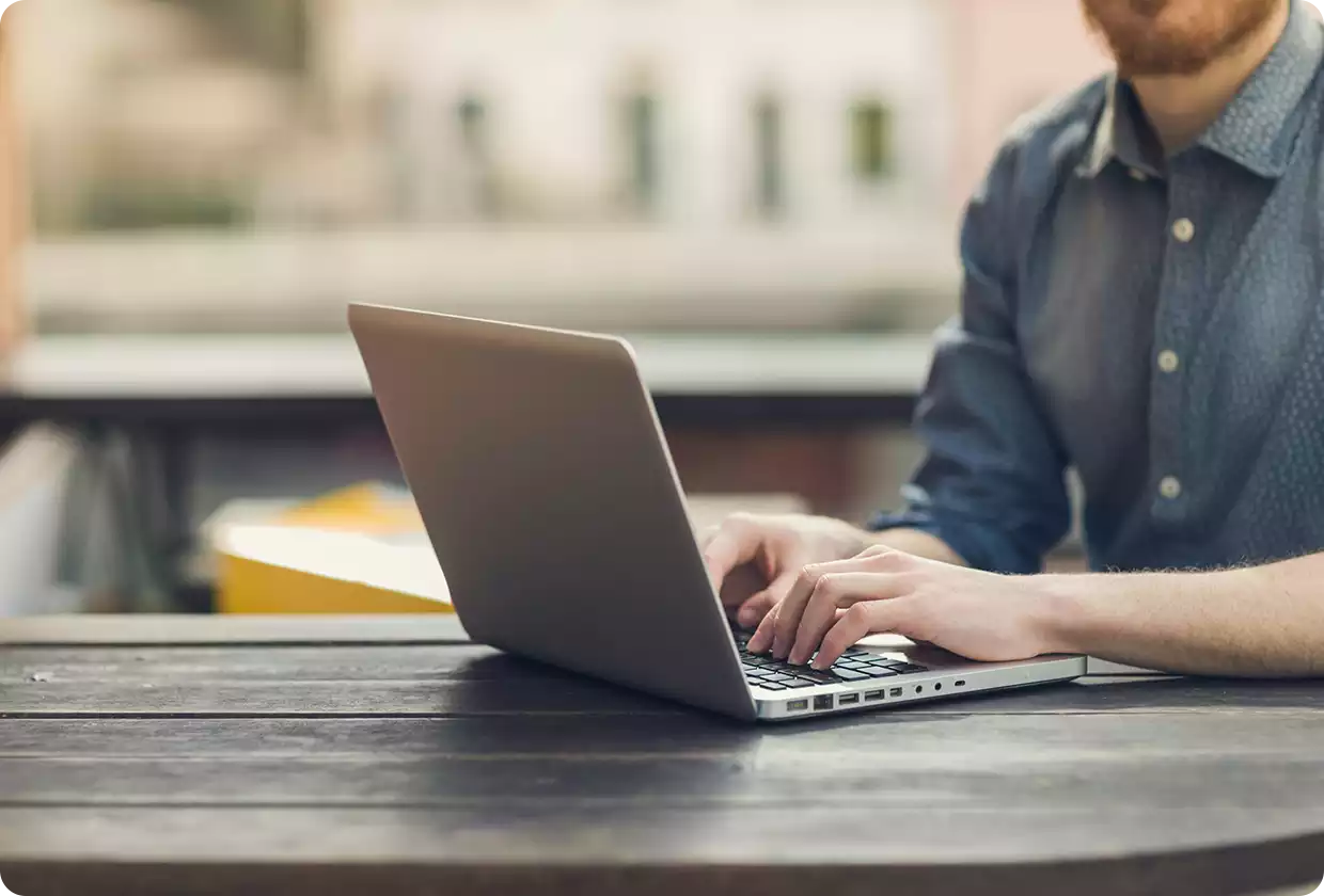 Person works on laptop on wooden table their face is not visible