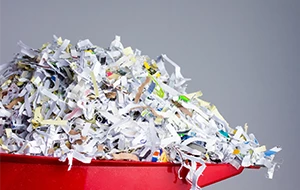 Red dustpan filled with shredded paper against a plain grey background.