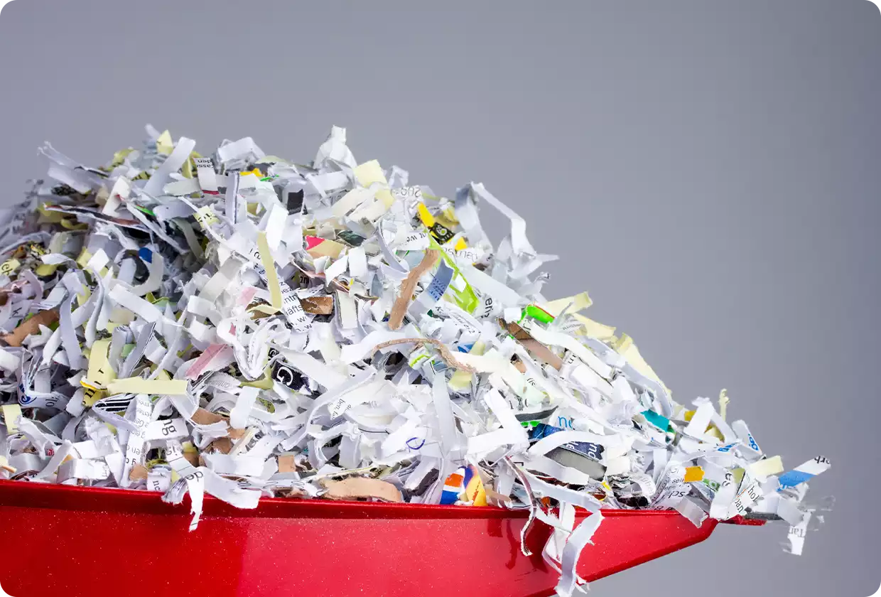 Red dustpan filled with shredded paper against a plain grey background