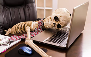Skeleton wearing a tie collapsed in front of a computer
