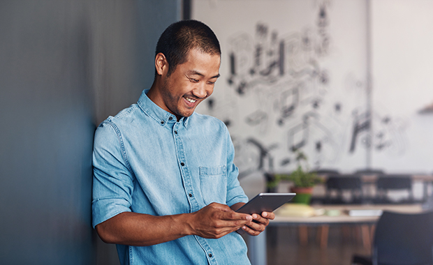 Smiling man leaning against wall looking at Android device