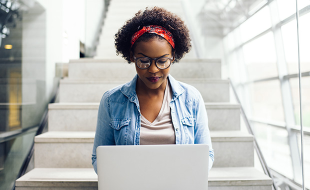 Focused African-American student sitting on stairs using a laptop