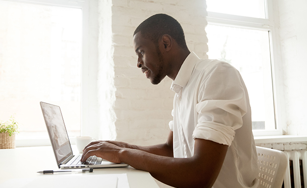 Side view of man sitting at desk working on laptop